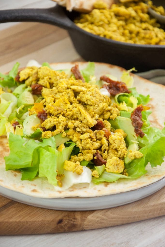 tofu scramble in an open-faced wrap with lettuce, avocado, and dried tomatoes