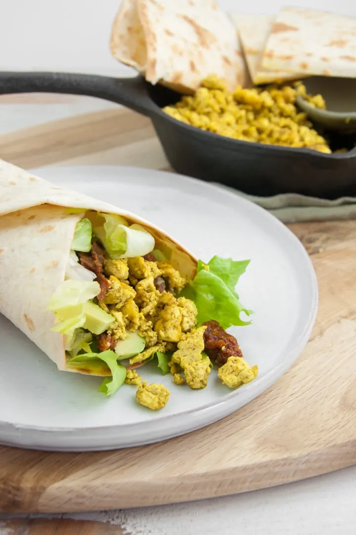 tofu scramble in a wrap with lettuce, avocado, and dried tomatoes