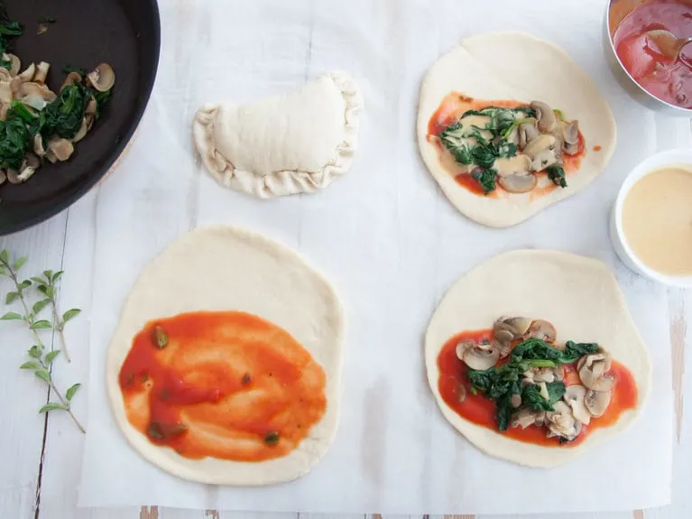 Assembling vegan mini calzones with tomato sauce, homemade cheese sauce, mushrooms and spinach