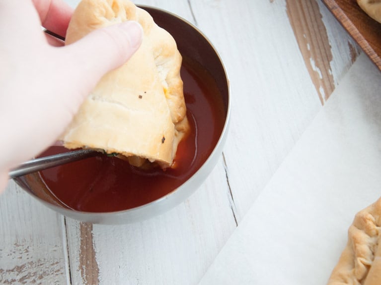 Vegan Mini Calzone filled with spinach and mushrooms being dipped in tomato sauce