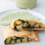 Vegan Potato and Spinach Strudel from the side with cilantro sunflower sauce in the background