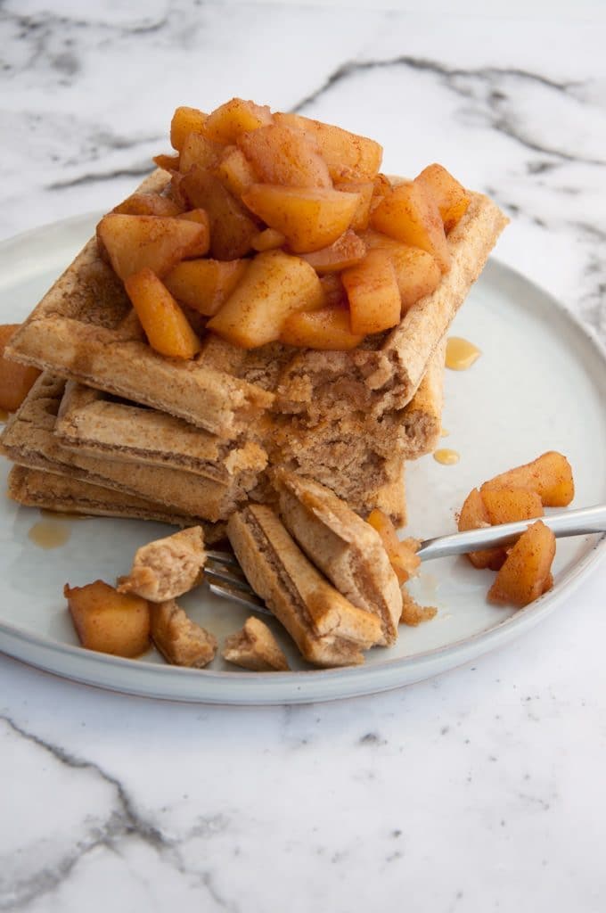 Vegan Cinnamon Waffles topped with warm Apple Sauce cut into with a fork