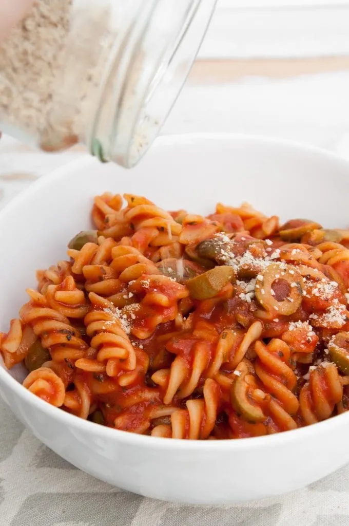 Sprinkling Almond Parmesan onto vegan Tomato Olive Pasta