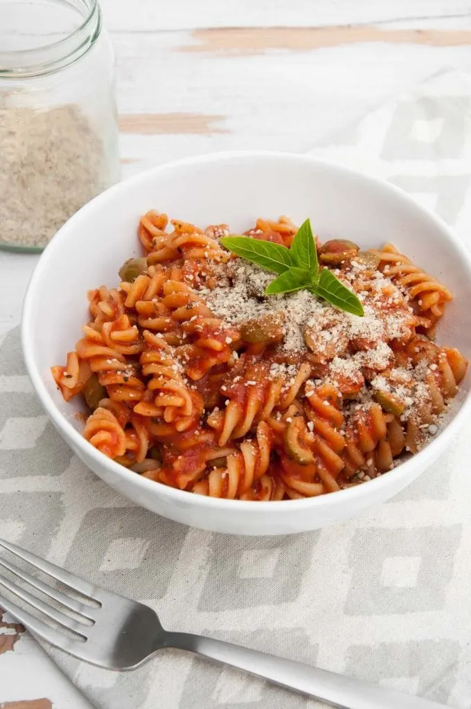 Pasta with tomato sauce and olives, garnished with fresh basil and almond parmesan