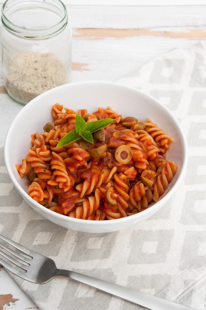 Pasta with tomato sauce and olives in a bowl with almond parmesan on the side