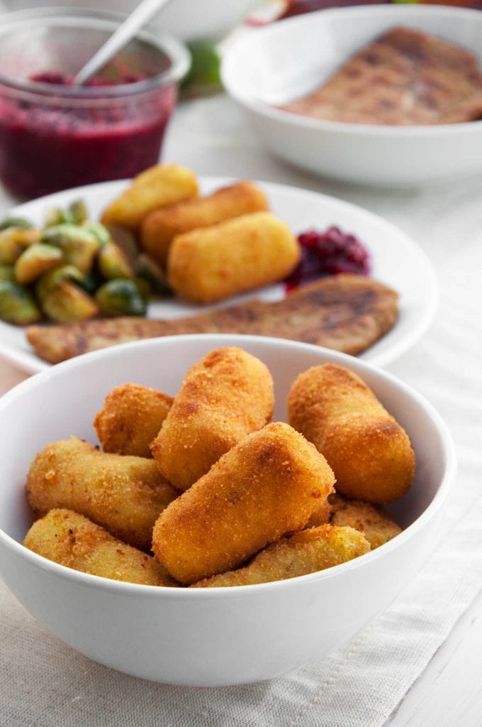 Vegan Potato Croquettes in a bowl with a plate of festive Thanksgiving food in the background