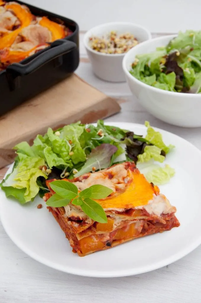 A piece of Pumpkin Lasagne with Cashew Cheese on a plate with side salad and shoots