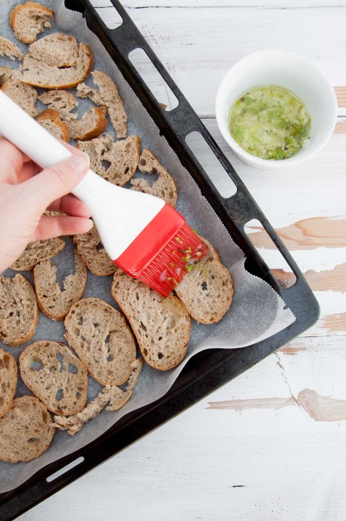 Crispy Bread Chips on a baking tray getting coated in garlic and herb oil