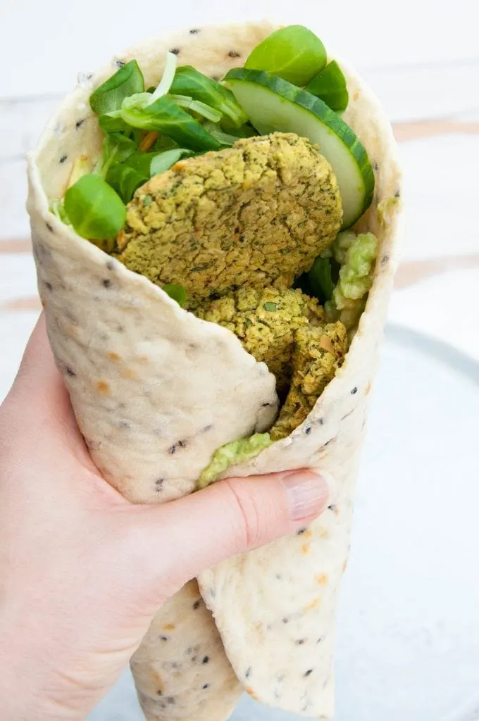 Green Goddess Wrap - Tortilla with salad, cucumber, avocado and spinach falafel in a hand
