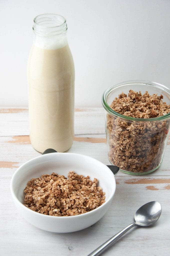 Vegan Gingerbread Granola in a bowl and glass jar with almond milk in the back