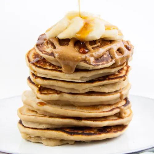 Vegan Protein Pancakes topped with peanut butter, banana slices and maple syrup