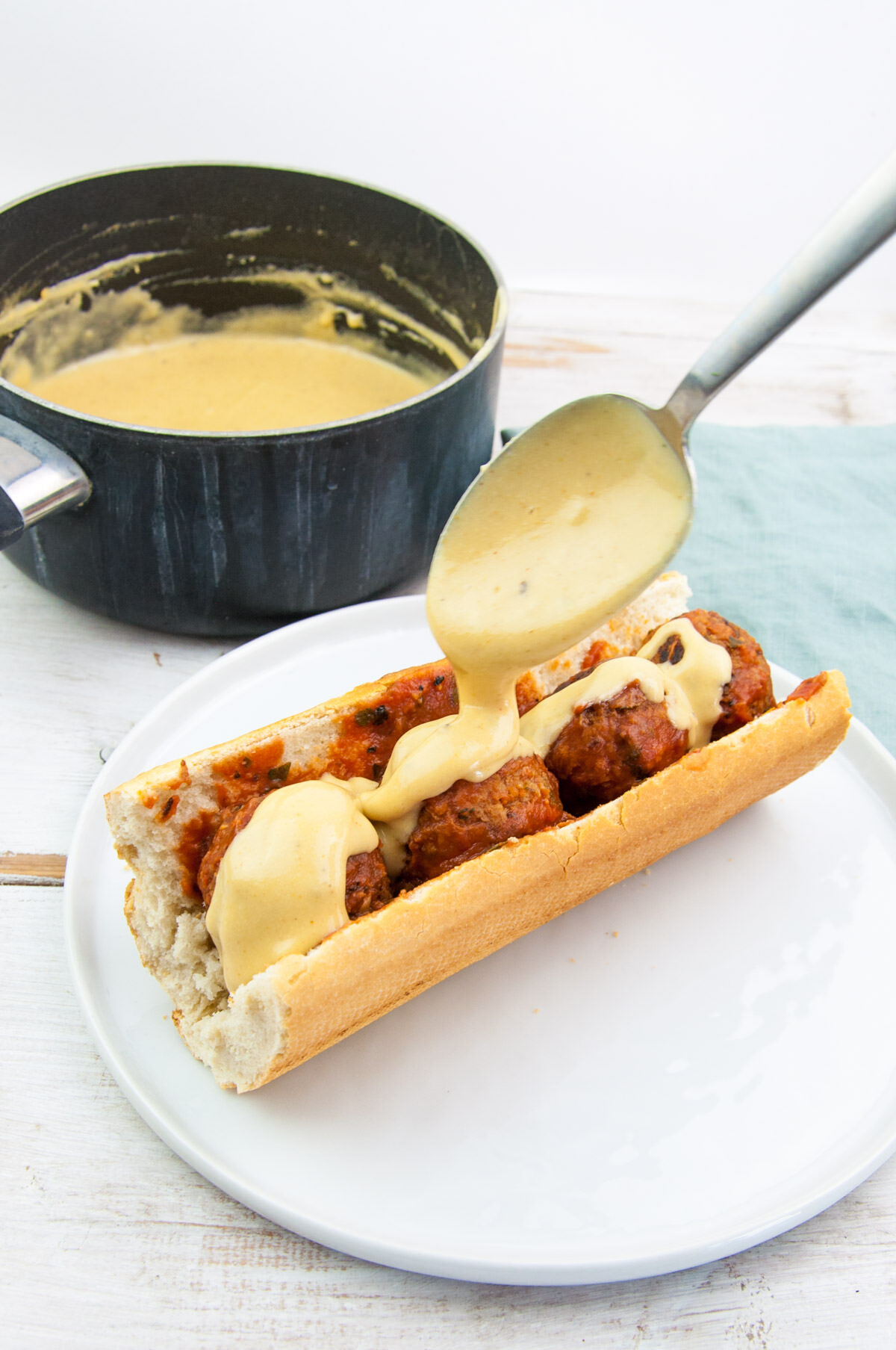 drizzling vegan cheese on meatball sub