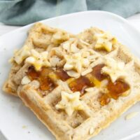 Vegan Banana Bread Waffles topped with maple syrup, banana slices, toasted almond slices and hazelnut meal