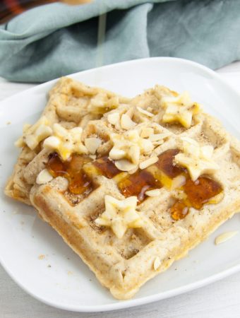 Vegan Banana Bread Waffles topped with maple syrup, banana slices, toasted almond slices and hazelnut meal