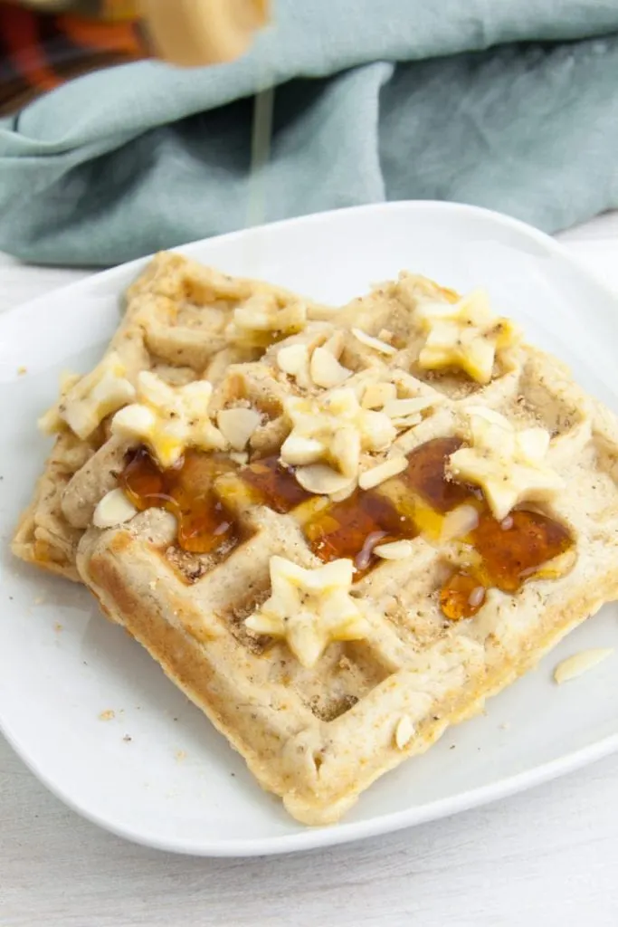Vegan Banana Bread Waffles topped with maple syrup, banana slices, toasted almond slices and hazelnut meal
