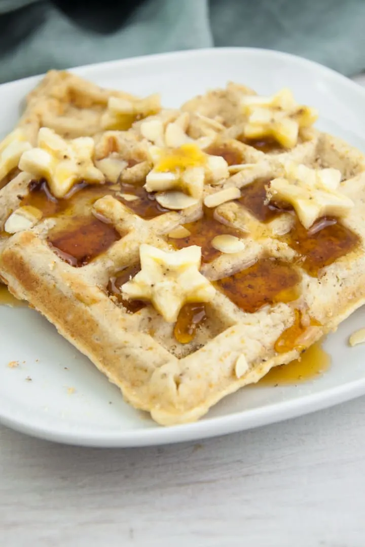 Vegan Banana Bread Waffles topped with maple syrup, banana slices, toasted almond slices and hazelnut meal