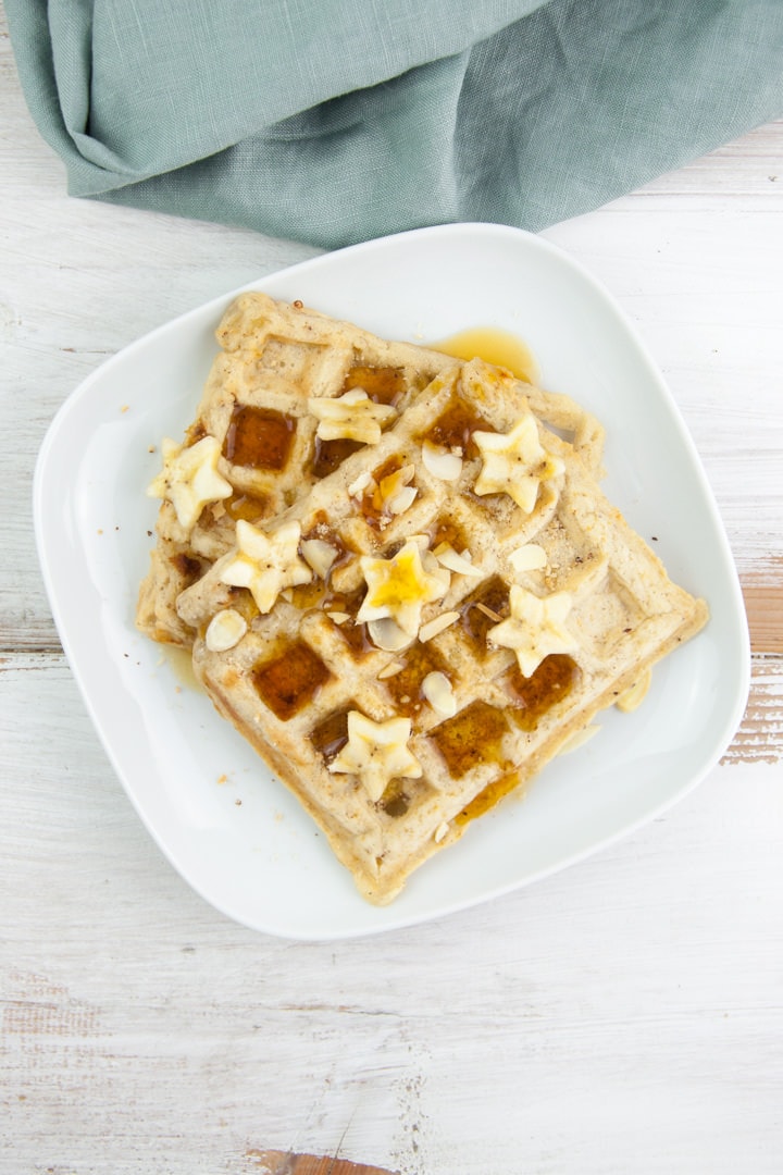 Vegan Banana Bread Waffles topped with maple syrup, banana slices, toasted almond slices and hazelnut meal