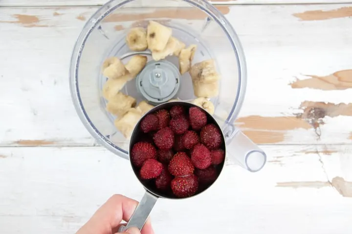 frozen strawberries in a cup and frozen bananas in a food processor
