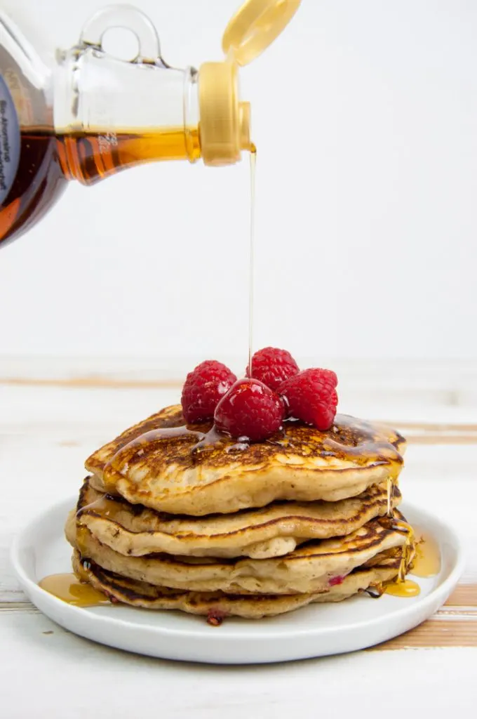 pouring maple syrup over vegan raspberry pancakes