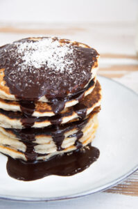 Vegan Coconut Pancakes topped with chocolate sauce and coconut flakes
