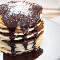 Vegan Coconut Pancakes topped with chocolate sauce and coconut flakes