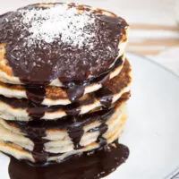 Vegan Coconut Pancakes topped with chocolate sauce and coconut flakes