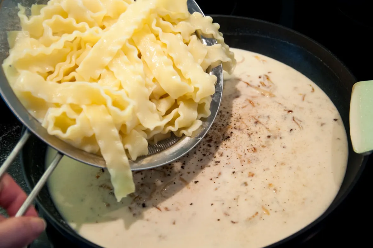 adding noodles to caramelized onions and cashew cream