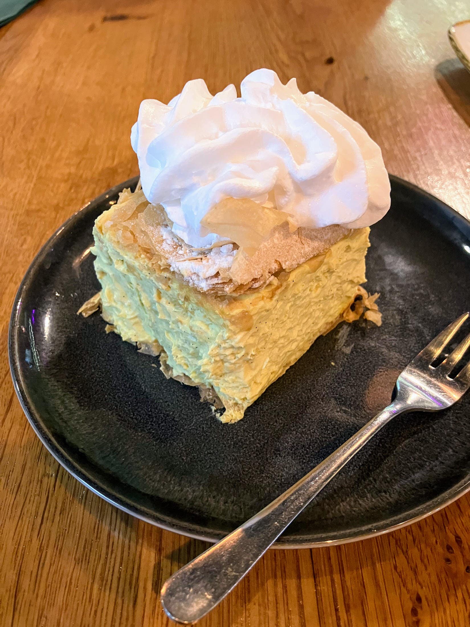 Vegan lemon cake with whipped cream on black plate at Elephantastic Vegan.